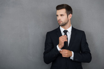 44203290 - perfect to the last detail. handsome young businessman adjusting his sleeves while standing against grey background